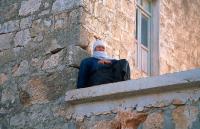 Starsza kobieta siedząc na tarasie swojego domu obserwuje drogę wjazdową do wsi Banabil.